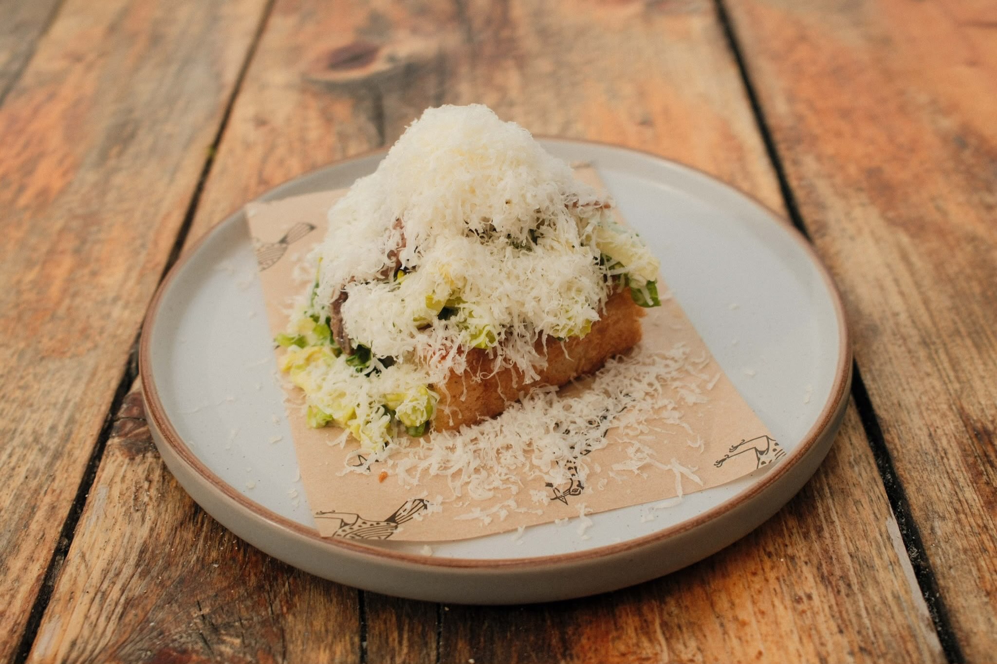 A golden breaded dish topped with shredded greens and finely grated cheese on a ceramic plate