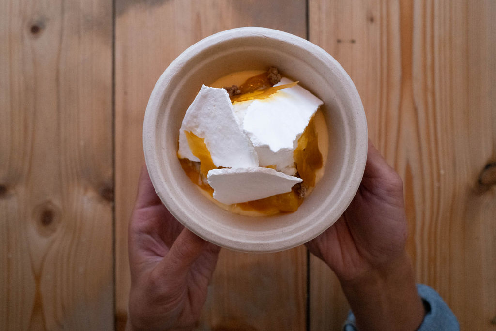 Hands holding a bowl of orange dessert topped with white meringue shards