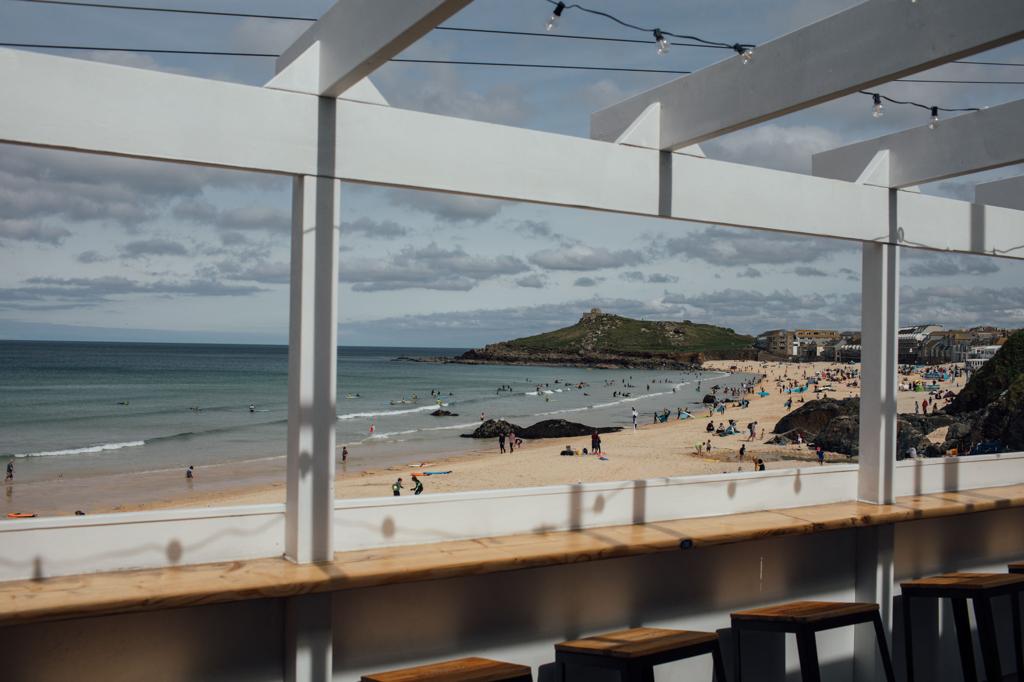 Porthmeor Beach and its rocky headland viewed through the white beams of The Fish Shed terrace